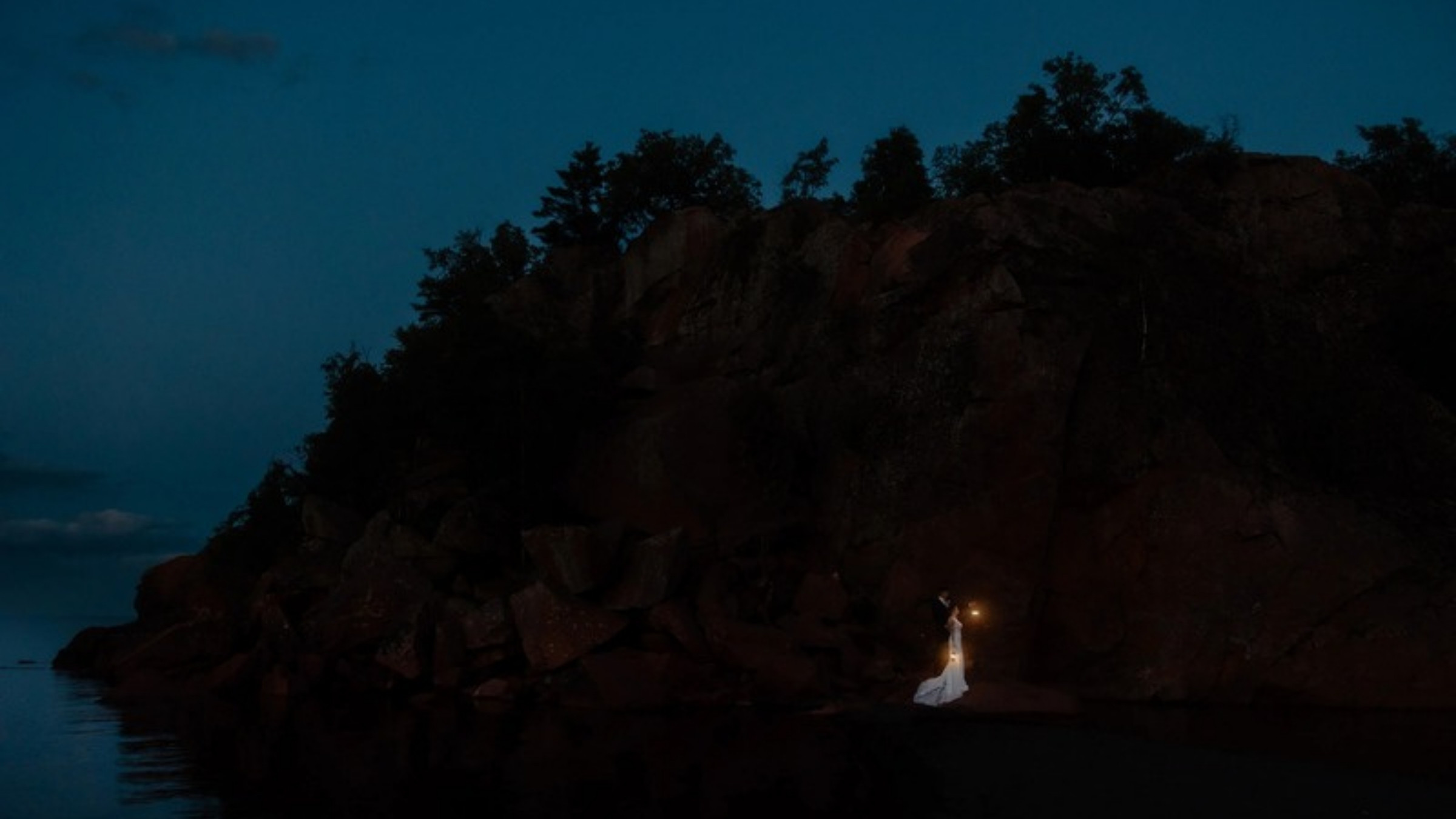 Bride holding a lantern on a dark Lake Superior cliff at blue hour, photographed by Samantha Burke Photography