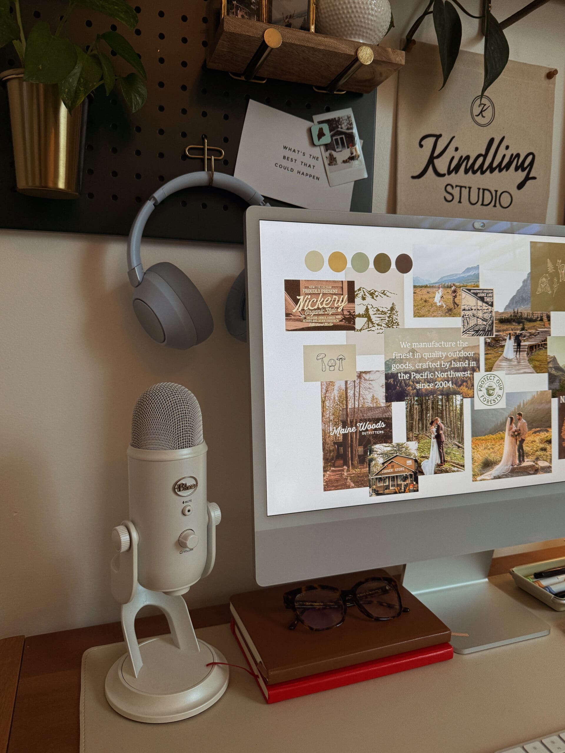 A warm, modern workspace with a computer displaying a mood board and color palette, surrounded by creative tools including a microphone, notebooks, and Kindling Studio wall art. The setup reflects the DIY branding process for a Showit website template.